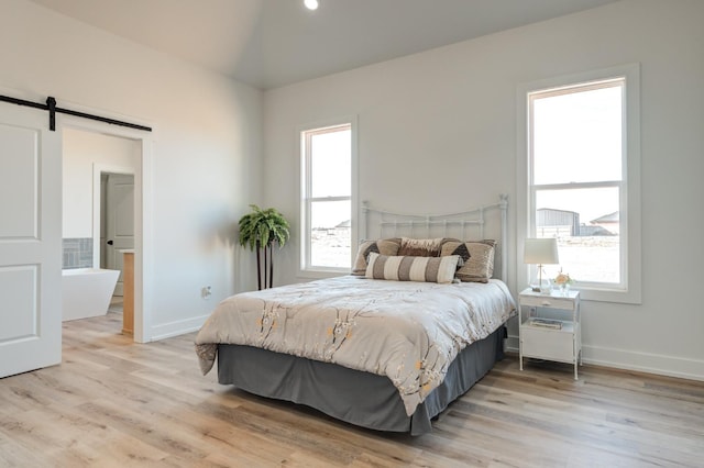 bedroom featuring a barn door, vaulted ceiling, multiple windows, and light hardwood / wood-style flooring