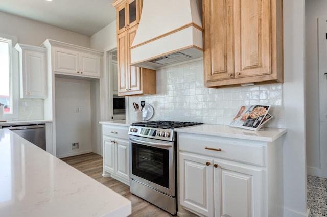 kitchen with custom range hood, stainless steel appliances, light stone countertops, light hardwood / wood-style floors, and decorative backsplash