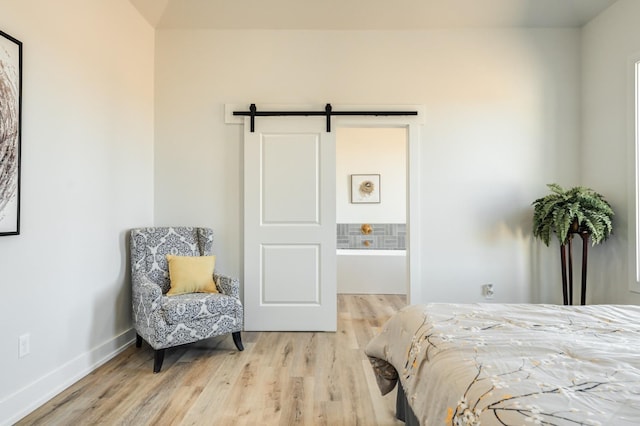 bedroom with ensuite bathroom, a barn door, and light hardwood / wood-style flooring