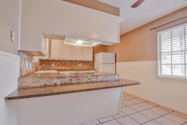 kitchen with sink, light tile patterned floors, kitchen peninsula, white fridge, and backsplash