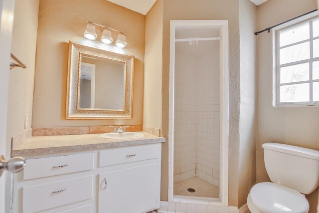 bathroom featuring a tile shower, vanity, and toilet