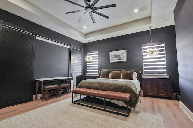 bedroom with light hardwood / wood-style flooring, a barn door, and ceiling fan