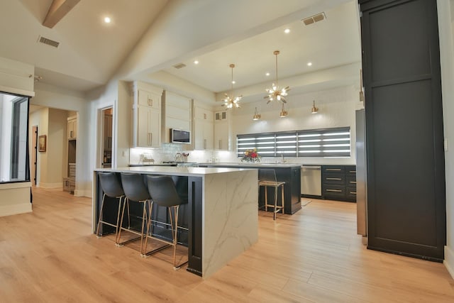 kitchen with a kitchen island, appliances with stainless steel finishes, white cabinetry, a kitchen breakfast bar, and hanging light fixtures