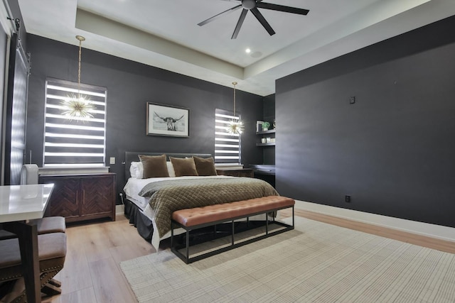 bedroom with a tray ceiling, light hardwood / wood-style floors, and ceiling fan