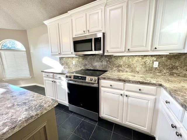 kitchen featuring white cabinetry, stainless steel appliances, light stone countertops, a textured ceiling, and dark tile patterned flooring