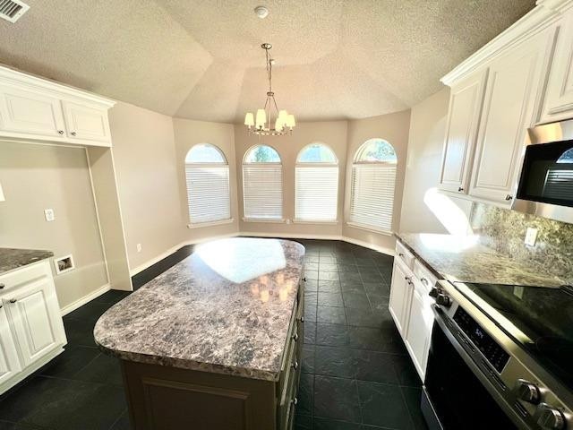 kitchen with white cabinetry, vaulted ceiling, light stone countertops, and appliances with stainless steel finishes