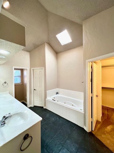 bathroom featuring vanity, tiled bath, a textured ceiling, and lofted ceiling with skylight