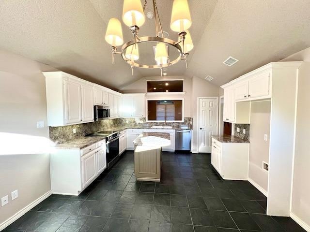 kitchen with stainless steel appliances, white cabinetry, vaulted ceiling, and dark stone countertops