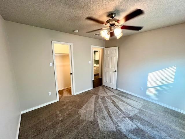 unfurnished bedroom with a walk in closet, dark carpet, ceiling fan, a textured ceiling, and a closet