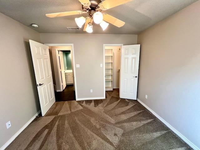 unfurnished bedroom with dark colored carpet, a spacious closet, a textured ceiling, a closet, and ceiling fan