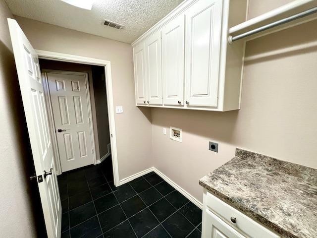 clothes washing area with dark tile patterned floors, cabinets, hookup for a washing machine, electric dryer hookup, and a textured ceiling