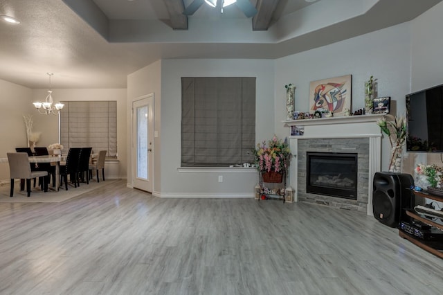 living room with beamed ceiling, a raised ceiling, hardwood / wood-style flooring, a fireplace, and ceiling fan with notable chandelier