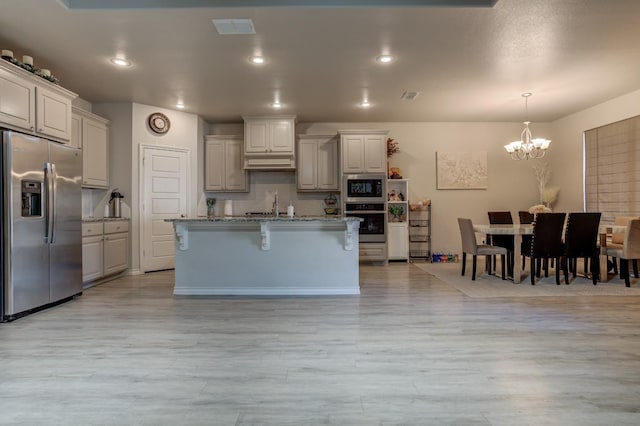 kitchen with a breakfast bar, hanging light fixtures, stainless steel appliances, light stone countertops, and a center island with sink