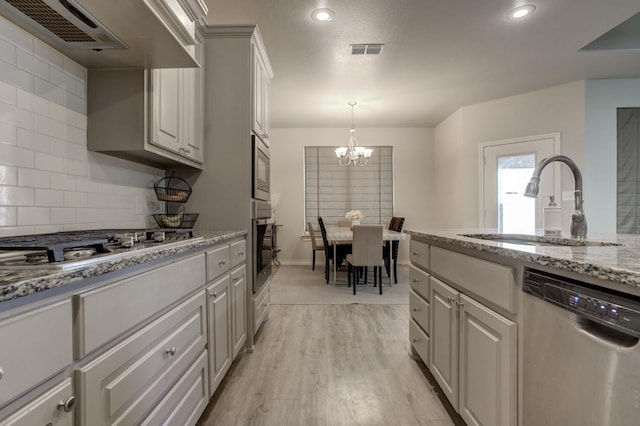 kitchen featuring sink, light wood-type flooring, appliances with stainless steel finishes, wall chimney range hood, and backsplash