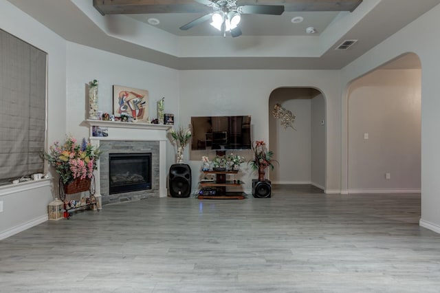 unfurnished living room with hardwood / wood-style flooring, ceiling fan, a tray ceiling, and a stone fireplace