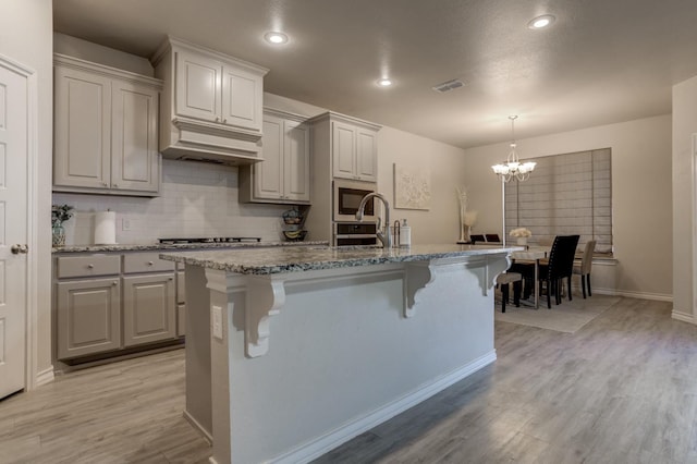 kitchen with built in microwave, light hardwood / wood-style floors, a kitchen breakfast bar, and an island with sink