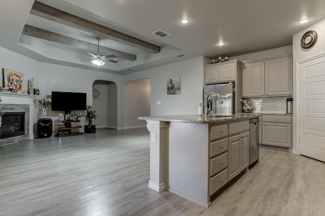 kitchen featuring decorative backsplash, stainless steel fridge, a center island with sink, and light wood-type flooring