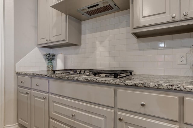 kitchen with tasteful backsplash, light stone counters, ventilation hood, stainless steel gas stovetop, and white cabinets