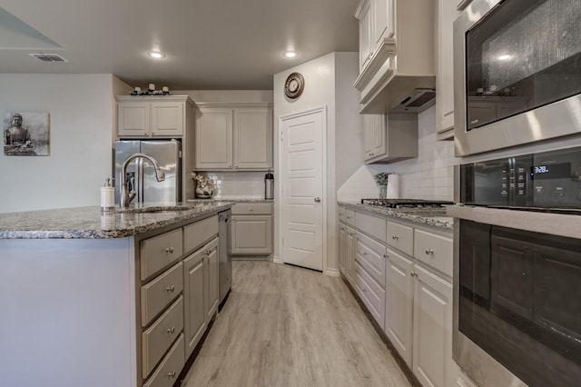 kitchen with tasteful backsplash, stainless steel appliances, light hardwood / wood-style floors, and a center island with sink