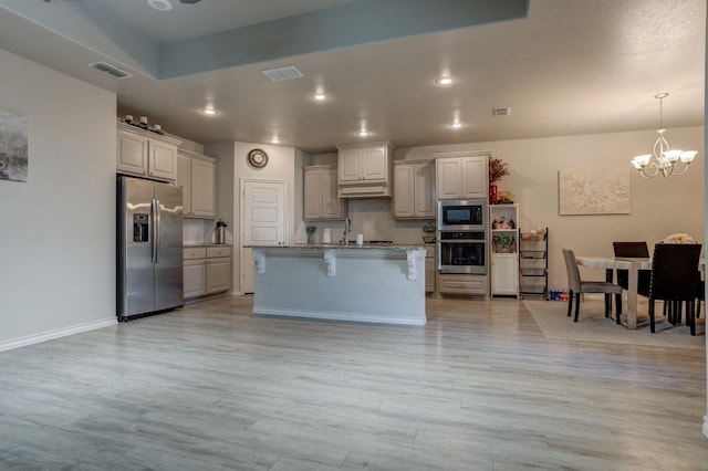 kitchen featuring a breakfast bar, an inviting chandelier, stainless steel appliances, light stone counters, and an island with sink