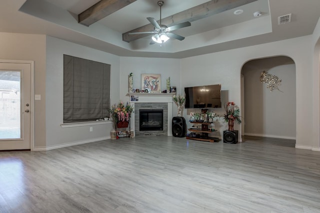 living room with ceiling fan, a fireplace, a tray ceiling, and light wood-type flooring