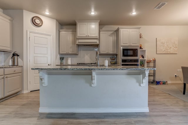 kitchen featuring built in microwave, extractor fan, a kitchen island with sink, and oven