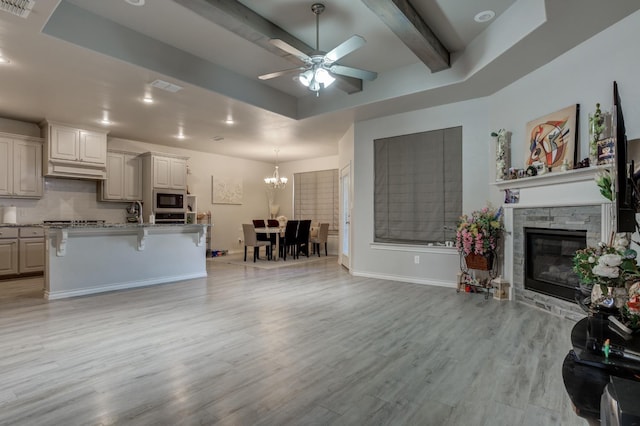 living room with a fireplace, beam ceiling, ceiling fan with notable chandelier, and light wood-type flooring