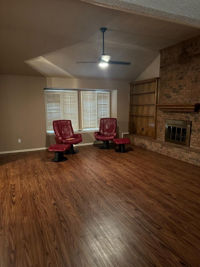 unfurnished room with lofted ceiling, hardwood / wood-style flooring, ceiling fan, a fireplace, and a textured ceiling