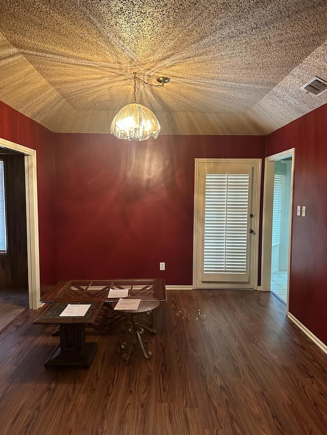 unfurnished dining area featuring lofted ceiling, a notable chandelier, dark wood-type flooring, and a textured ceiling