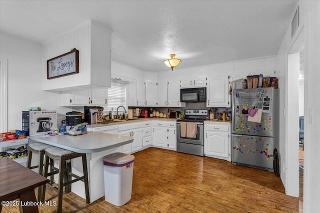 110 E 18th St, Littlefield, TX 79339 - kitchen featuring freestanding refrigerator, electric range, black microwave, a peninsula, and white cabinetry