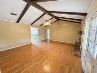 unfurnished living room featuring a healthy amount of sunlight, hardwood / wood-style floors, lofted ceiling with beams, and ceiling fan