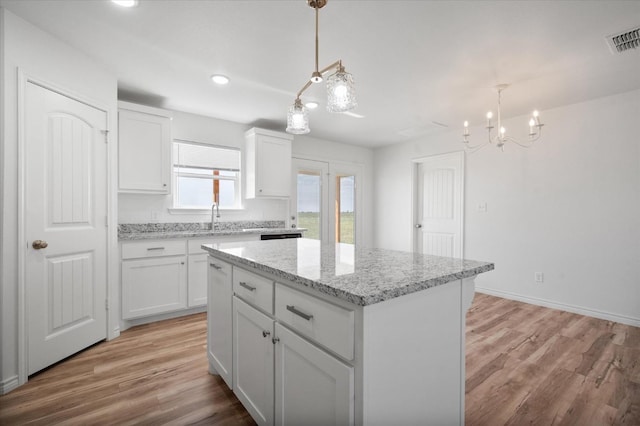 kitchen with white cabinetry, light stone counters, decorative light fixtures, a center island, and light hardwood / wood-style flooring