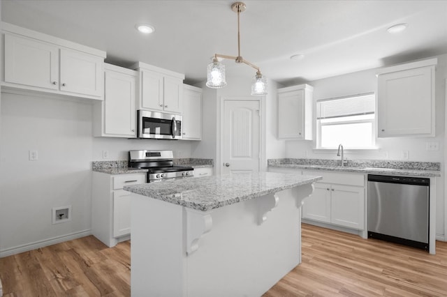 kitchen featuring white cabinetry, appliances with stainless steel finishes, a center island, and decorative light fixtures