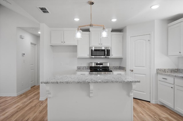 kitchen featuring appliances with stainless steel finishes, a kitchen island, pendant lighting, light stone countertops, and white cabinets