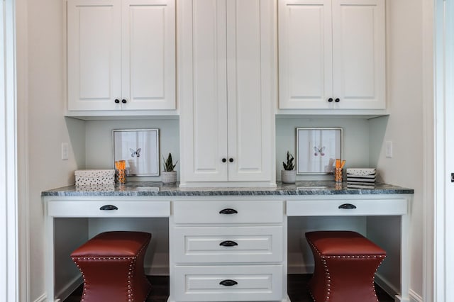 bar featuring white cabinetry, built in desk, and dark stone countertops