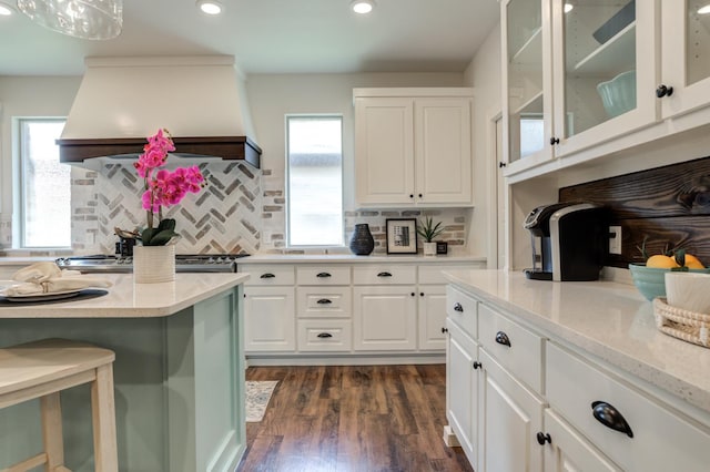 kitchen featuring premium range hood, white cabinetry, backsplash, light stone countertops, and dark hardwood / wood-style flooring