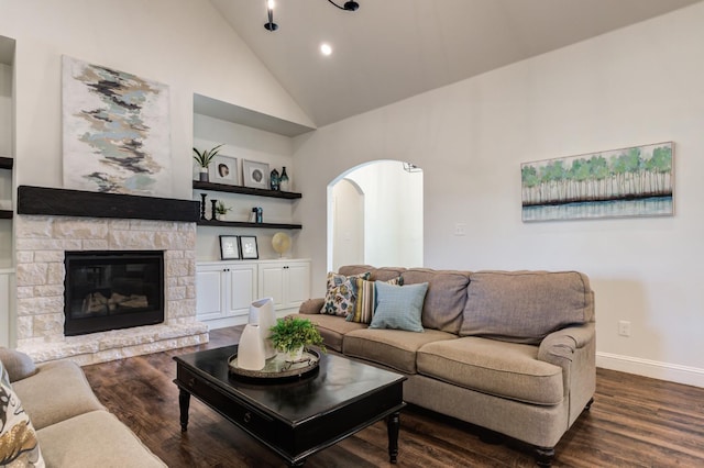 living room featuring dark hardwood / wood-style flooring, high vaulted ceiling, and a stone fireplace