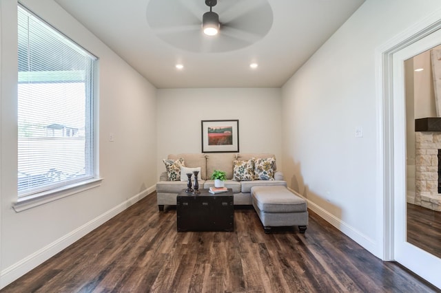 sitting room featuring a stone fireplace, dark wood-type flooring, and ceiling fan