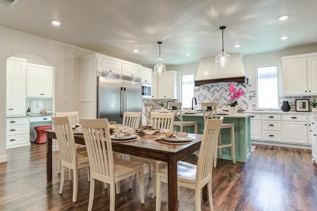 kitchen with pendant lighting, dark wood-type flooring, stainless steel built in refrigerator, white cabinets, and a kitchen island