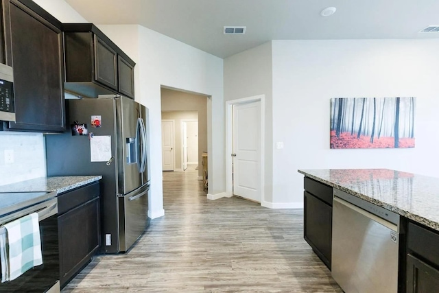 kitchen featuring stainless steel appliances, light stone countertops, dark brown cabinets, and light wood-type flooring