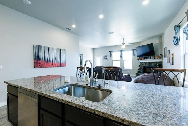 kitchen featuring stainless steel dishwasher, a fireplace, light stone countertops, and sink