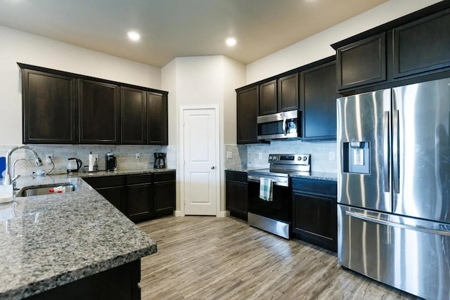 kitchen featuring stainless steel appliances, sink, backsplash, and light stone counters