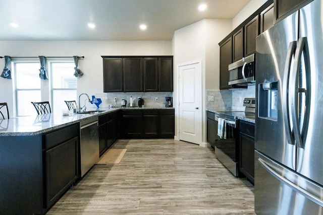 kitchen with sink, decorative backsplash, light stone counters, stainless steel appliances, and light wood-type flooring