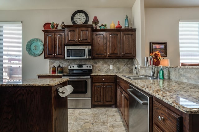 kitchen with appliances with stainless steel finishes, sink, backsplash, light stone counters, and dark brown cabinets