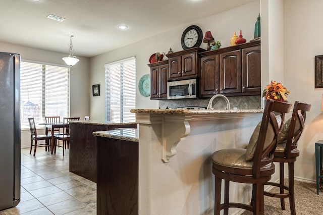 kitchen featuring light stone counters, stainless steel appliances, a kitchen bar, and hanging light fixtures