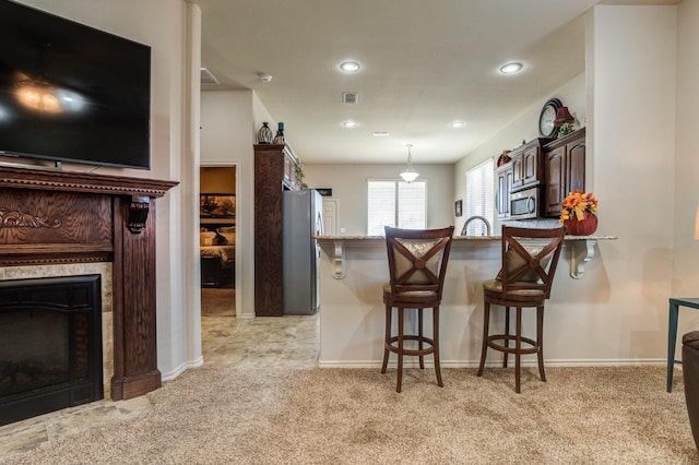 kitchen featuring a tile fireplace, a breakfast bar, appliances with stainless steel finishes, dark brown cabinetry, and light colored carpet