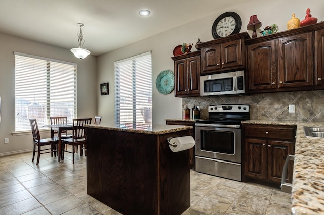 kitchen with dark brown cabinets, hanging light fixtures, a kitchen island, stainless steel appliances, and light stone countertops