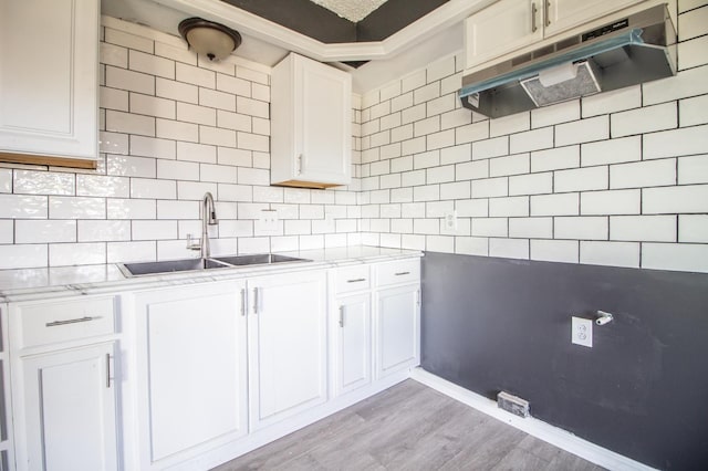 kitchen with white cabinetry, sink, backsplash, light stone counters, and light wood-type flooring