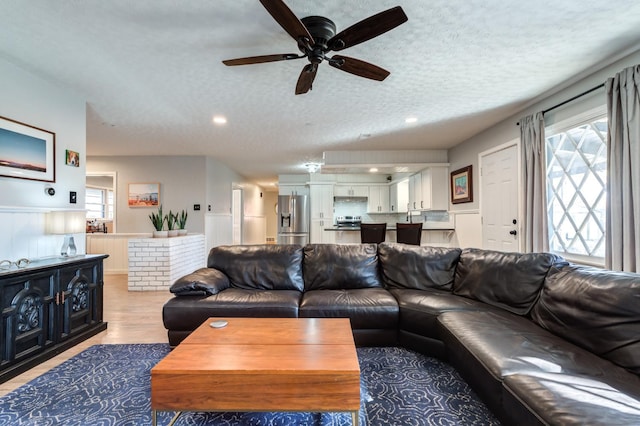 living room with ceiling fan, a healthy amount of sunlight, a textured ceiling, and light wood-type flooring