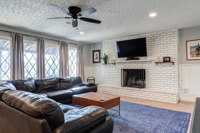 living room featuring hardwood / wood-style floors, a fireplace, a textured ceiling, and ceiling fan